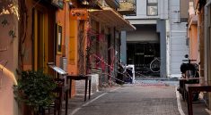 Explore a quaint alleyway in Athens, Greece, featuring inviting cafés and warm colors on a sunny day.